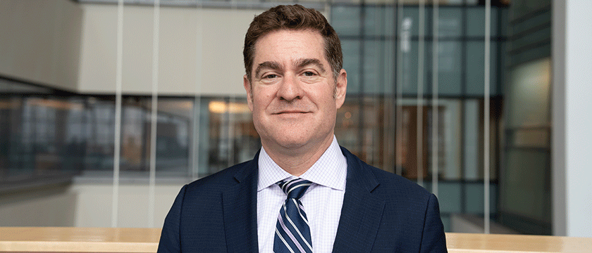Headshot of a Baruch College professor wearing a business suit standing inside the main atrium of the campus.