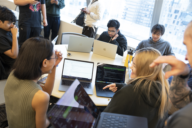 students sit by desk with open laptops